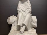 une statue blanche représentant une jeune fille assise sur un rocher