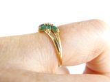 a woman ' s hand holding a gold ring with a green stone