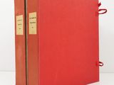 an old red book with a red cover sitting on top of a white table