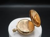 a small gold pocket watch sitting on top of a white pedestal