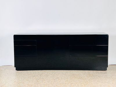 une commode noire posée sur un sol beige, près d'un mur blanc