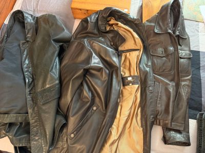 une veste en cuir noire et une veste en cuir marron posées sur un lit