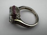a close up of a diamond and ruby ring on a white surface