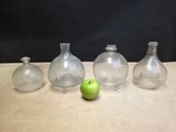 four glass vases and a green apple on a table