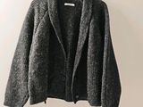 un cardigan gris suspendu à un cintre devant un mur blanc
