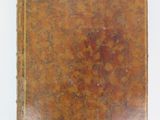 an old brown book sitting on top of a table next to a white wall