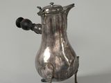 an antique silver coffee pot sitting on a stand on a white surface