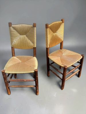 pair of wooden chairs with woven seats against a gray background