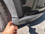 a person holding a piece of metal near the front bumper of a car