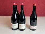 trois bouteilles de vin sont posées sur une table devant un mur rouge