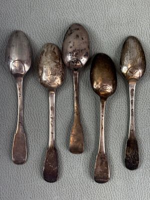 five silver spoons are lined up on a gray surface