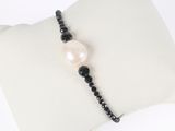 a close up of a bracelet with a pearl and black beads