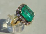 an image of a ring with a green emerald surrounded by white diamonds