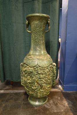 un grand vase vert posé par terre devant un rideau