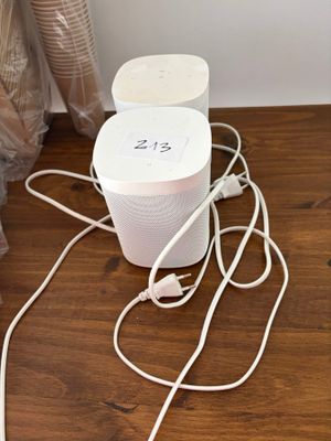 une enceinte blanche posée sur un parquet, à côté d'un rideau