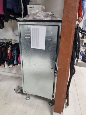 un petit réfrigérateur dans un coin d'une pièce, avec des vêtements sur les étagères