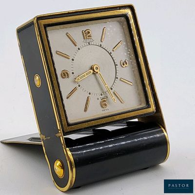 une horloge noire et dorée posée sur un socle, sur une surface blanche