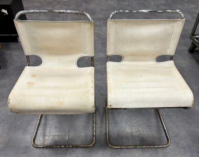 une paire de fauteuils en cuir blanc avec des pieds en métal, dans un entrepôt