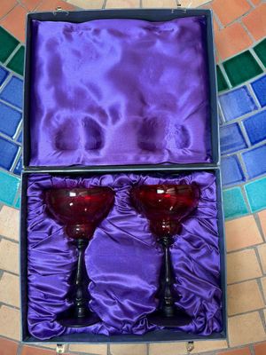 une paire de verres à vin rouge dans une boîte violette, posée sur un sol carrelé
