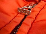 an orange jacket with a metal zipper and a name tag on it