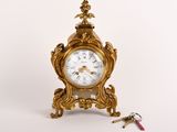 une petite horloge en or posée sur une table, avec un trousseau de clés à côté