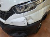 the front end of a white van with a dent in it ' s bumper