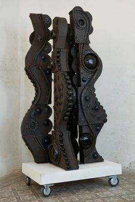 une sculpture noire posée sur un socle blanc, au milieu d'un sol carrelé