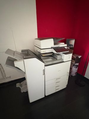une imprimante blanche posée sur un bureau, près d'un mur rouge