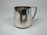 a silver pitcher on a white surface with a red handle