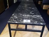 une table en marbre noir avec un piètement en métal, posée à même le sol