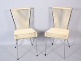 pair of white chairs with metal legs against a white wall