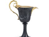 une coupe ancienne noire et dorée, munie d'anses et posée sur un socle