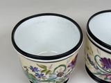 two cups with flowers painted on them sitting on a table