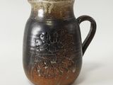 une tasse noire et marron avec une anse, posée sur une surface blanche
