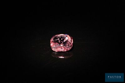un diamant rose sur une surface noire dans l'obscurité