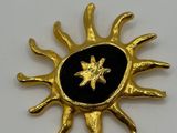 an image of a gold and black sun broochle on a white surface