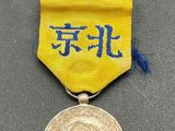 un ruban jaune portant une inscription en chinois et une médaille d'or posée sur un fond gris