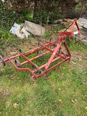 an old red plow sitting on top of a lush green field