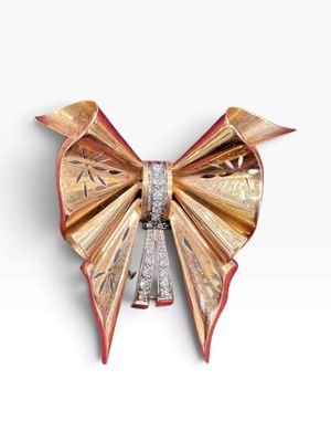 a gold and diamond bow brooch on a white surface