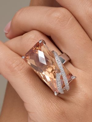 une image représentant la main d'une femme tenant une bague sertie d'un diamant orange