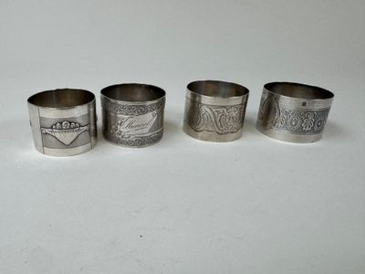 four silver napkin rings with designs on them on a white surface