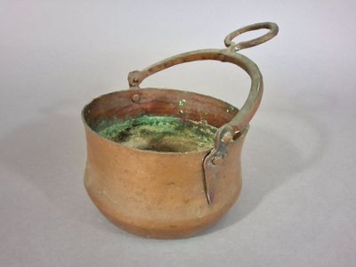une petite casserole en cuivre avec une poignée, posée sur une surface blanche