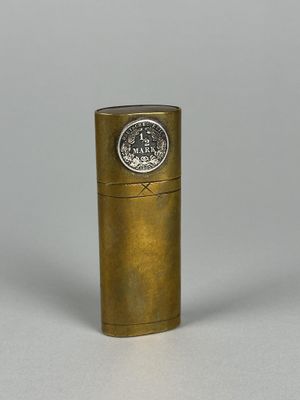 un vieux briquet en laiton avec un capuchon métallique posé sur une surface blanche