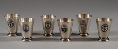 six silver cups with crest emblems are lined up on a table