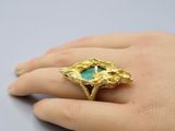 une image représentant la main d'une femme portant une bague en or sertie d'une pierre turquoise