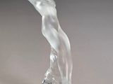 sculpture représentant une figure féminine posée sur un socle transparent, sur fond gris