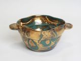 a gold and green bowl with handles on a white surface