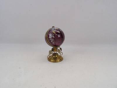 globe en verre violet posé sur un socle doré, sur une surface blanche