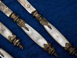 four silverware knives with ornate designs on them on a blue cloth