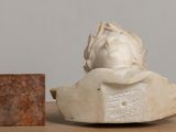 a statue of a woman sitting on a chair next to a block of wood
